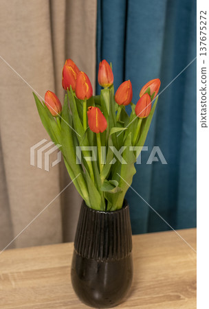 a bouquet of orange and red tulips, arranged in a dark, ribbed vase for home decor. a bouquet of orange and red tulips, arranged in a dark, ribbed vase for home decor. 137675272