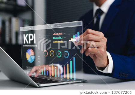 Business KPI concept. Professional businessman using a laptop to analyze key performance indicators on a digital dashboard, with financial charts, bar graphs, a tracking monitor, and data analytics. 137677205