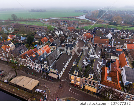 Aerial view of the historic town of Muiden, Netherlands, showing traditional brick houses, cobblestone streets, and the defensive Muizenfort fortification under a misty morning sky. Aerial view of the historic town of Muiden, Netherlands, showing traditional brick houses, cobblestone streets, and the defensive Muizenfort fortification under a misty morning sky. 137677282