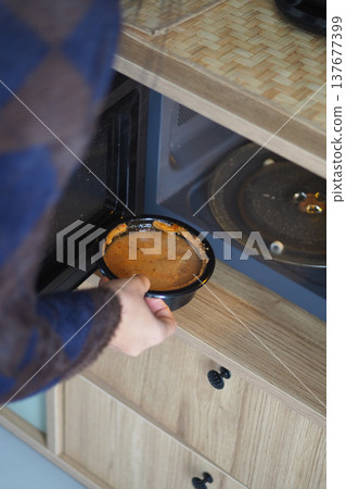 Person removes bowl from microwave in kitchen Person removes bowl from microwave in kitchen 137677399