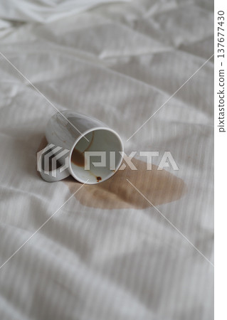 Coffee cup spills on a white bed sheet in morning light Coffee cup spills on a white bed sheet in morning light 137677430
