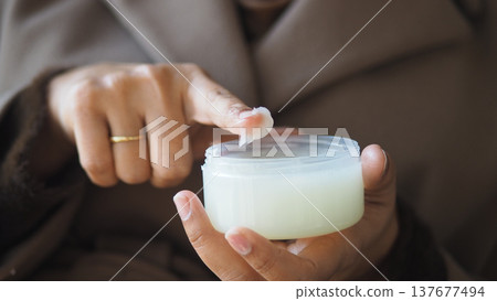 A person uses a finger to apply petroleum jelly from a small container indoors A person uses a finger to apply petroleum jelly from a small container indoors 137677494