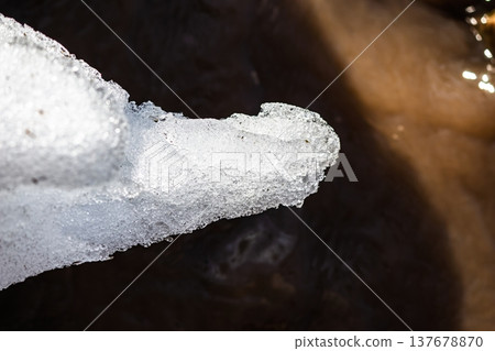 Macro shot of glistening, textured melting ice by a bubbling spring stream. Hints of slush and flowing water herald the vibrant arrival of early spring 137678870