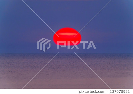 A fantastical scene of a giant red Daruma-shaped sunset floating on the horizon and the tranquil sea. A fantastical scene of a giant red Daruma-shaped sunset floating on the horizon and the tranquil sea. 137678931