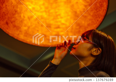 A woman's profile as she gazes at an orange light. 137679289