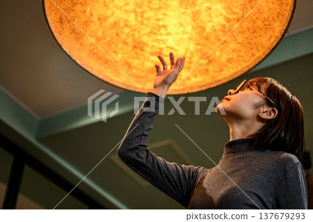 A woman reaches out to a large light fixture. A woman reaches out to a large light fixture. 137679293