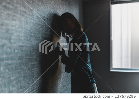 Silhouette of a woman leaning against a wall, lost in thought (cinematic photograph) 137679299