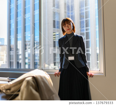 一位身穿西裝的女士在辦公室窗前擺姿勢拍照。 137679333