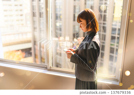 一位女士在窗邊看著她的智慧型手機。 137679336