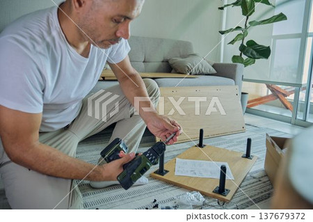 Man assembling flat pack furniture using a power drill Man assembling flat pack furniture using a power drill 137679372