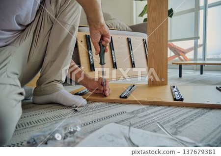 Person assembling flat pack furniture using screwdriver at home Person assembling flat pack furniture using screwdriver at home 137679381