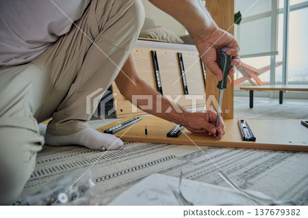 Man assembling wooden furniture using a screwdriver at home Man assembling wooden furniture using a screwdriver at home 137679382