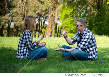 Father And Daughter Sitting On Grass In Summer Park Playing Rock Paper Scissors 137679533