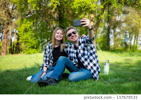 Happy Father And Daughter Taking A Selfie With A Smartphone, Sitting On The Grass In The Park Happy Father And Daughter Taking A Selfie With A Smartphone, Sitting On The Grass In The Park 137679535
