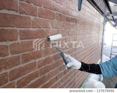 一位工匠正在用滾筒粉刷房屋外牆。 一位工匠正在用滾筒粉刷房屋外牆。 137679898