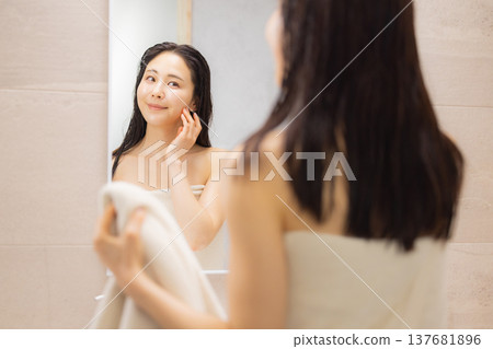 A woman doing skincare and hair care in the bathroom. 137681896