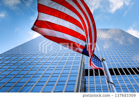 American flag waves in front of tall building under blue sky busy urban area 137683309