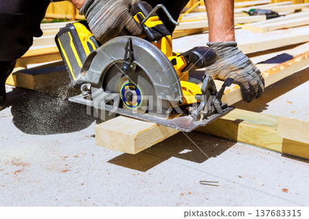 Hands use circular saw to cut wood at construction site 137683315