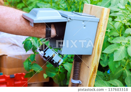 Hand connects electrical components inside gray box mounted on wooden post Hand connects electrical components inside gray box mounted on wooden post 137683318