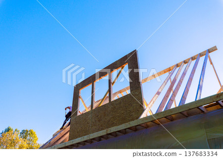 Construction worker builds roof structure with wooden beams in town environment Construction worker builds roof structure with wooden beams in town environment 137683334