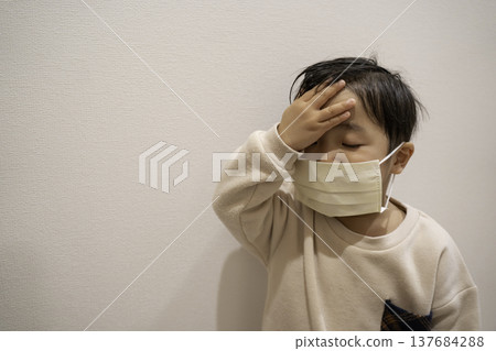 A child wearing a mask and covering their forehead. 137684288