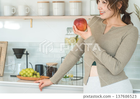 A woman eating an apple in her kitchen at home (diet, vegetarian) 137686523