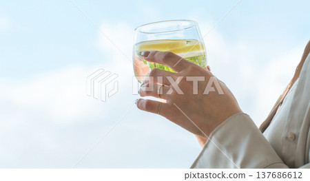 一位女士正在喝排毒水、檸檬水和薄荷水，她的手就放在她手上。 137686612