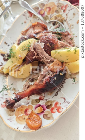 Roasted duck served with boiled potatoes and garnished with fresh herbs on an ornate platter, displayed on a table setting with elegant tableware Roasted duck served with boiled potatoes and garnished with fresh herbs on an ornate platter, displayed on a table setting with elegant tableware 137688007