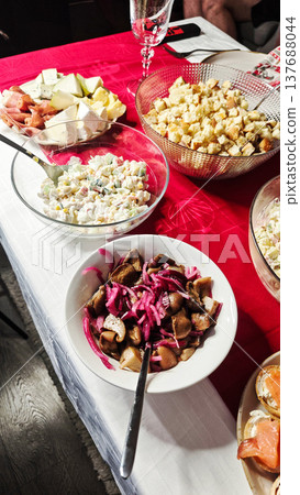 Colorful assortment of traditional dishes served on a festive table with red tablecloth, featuring salads, fruits, and pickled vegetables in various bowls Colorful assortment of traditional dishes served on a festive table with red tablecloth, featuring salads, fruits, and pickled vegetables in various bowls 137688044