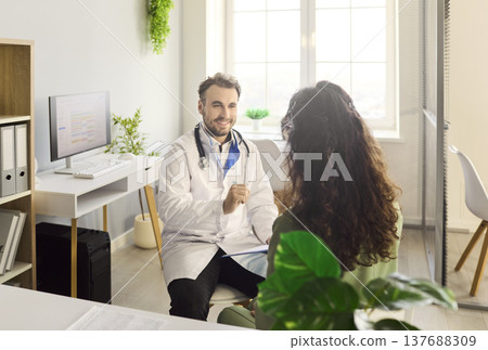 Smiling doctor advises female patient in bright clinic office during appointment Smiling doctor advises female patient in bright clinic office during appointment 137688309