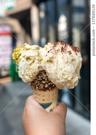 Hand holding Pistachio and Tiramisu Gelato, Ice-cream with waffle cone Hand holding Pistachio and Tiramisu Gelato, Ice-cream with waffle cone 137689126