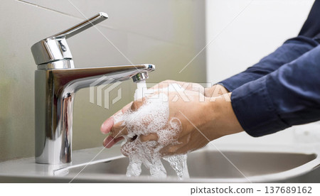 A man's hands are washing them. They are covered in soap suds. Water is running from the tap. A man's hands are washing them. They are covered in soap suds. Water is running from the tap. 137689162