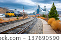 Freight train traveling past industrial factory along railway tracks 137690590
