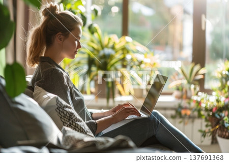 A young woman working on a laptop at home with sunlight streaming in surrounded by lush greenery and plants creating a serene workspace environment. Generative AI A young woman working on a laptop at home with sunlight streaming in surrounded by lush greenery and plants creating a serene workspace environment. Generative AI 137691368