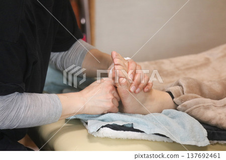 A woman giving a foot reflexology massage. 137692461