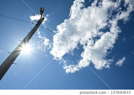 A telephone pole soaring against a blue sky, with the sun shining brightly – an image of urban infrastructure. A telephone pole soaring against a blue sky, with the sun shining brightly – an image of urban infrastructure. 137693633