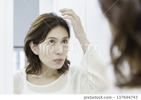 一位中年日本女性對著鏡子，為自己日漸稀疏的頭髮感到擔憂。 137694743