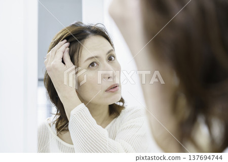 一位中年日本女性對著鏡子,為自己日漸稀疏的頭髮感到擔憂。 一位中年日本女性對著鏡子,為自己日漸稀疏的頭髮感到擔憂。 137694744