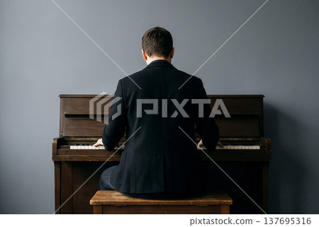 一位男士的背影,他正在彈奏一架古董直立式鋼琴。 一位男士的背影,他正在彈奏一架古董直立式鋼琴。 137695316