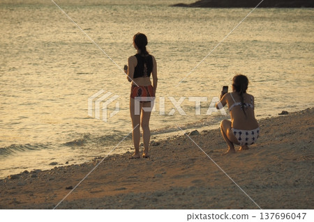 夕陽灑滿沙灘,一位穿著泳裝的女子:這是沖繩的一幕。 夕陽灑滿沙灘,一位穿著泳裝的女子:這是沖繩的一幕。 137696047