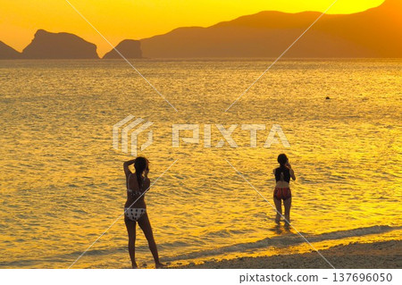 夕陽灑滿沙灘,一位穿著泳裝的女子:這是沖繩的一幕。 夕陽灑滿沙灘,一位穿著泳裝的女子:這是沖繩的一幕。 137696050