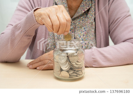 Retired elderly woman putting coins money in piggy bank and worry about monthly expenses and treatment fee payment. Retired elderly woman putting coins money in piggy bank and worry about monthly expenses and treatment fee payment. 137696180