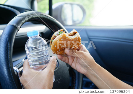 Asian woman driver hold and eat hamburger food in car. 137696204