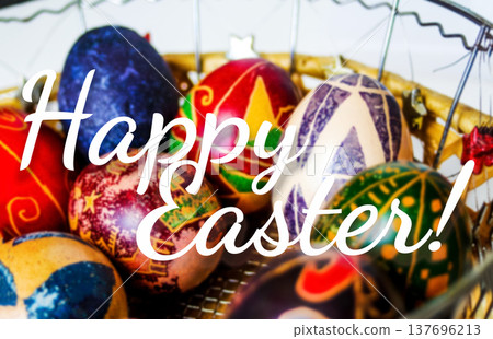 Happy Easter greeting card concept. Close-up of traditional painted Easter eggs pysanky in a wicker basket with elegant white Happy Easter text overlay Happy Easter greeting card concept. Close-up of traditional painted Easter eggs pysanky in a wicker basket with elegant white Happy Easter text overlay 137696213