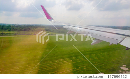 Plane wing extends over lush green fields 137696512