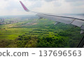 Airplane wing extends over lush green fields 137696563