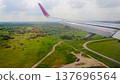 Airplane wing extends over lush green fields 137696564