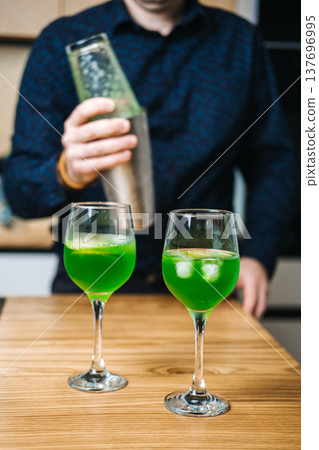 Mixing glass containing green liquid and cucumber slices sits on wooden counter next to metal shaker and lime slices. low alcohol cocktails, mindful drinking, sessionable drinks, lighter aperitifs Mixing glass containing green liquid and cucumber slices sits on wooden counter next to metal shaker and lime slices. low alcohol cocktails, mindful drinking, sessionable drinks, lighter aperitifs 137696995