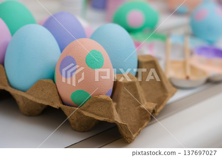 many colorful pastel decorated easter eggs in a brown paper carton and watercolor painting tool on table 137697027