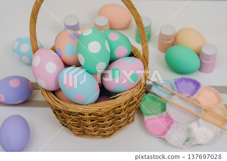 many colorful pastel decorated easter eggs in small wooden basket and watercolor painting tool on table 137697028